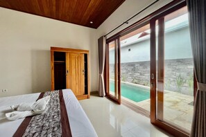 A hotel room with a bed, a wooden wardrobe, a sliding glass door leading to a pool area. - Belvilla Tirta Sari Resort Central Ubud (Ubud)