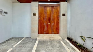 A wooden double door with a modern design, flanked by two small square windows, leading to a tiled entrance area. - Belvilla Tirta Sari Resort Central Ubud (Ubud)