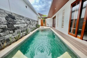 A swimming pool with a stone wall on one side and wooden deck on the other, leading to a wooden door. - Belvilla Tirta Sari Resort Central Ubud (Ubud)