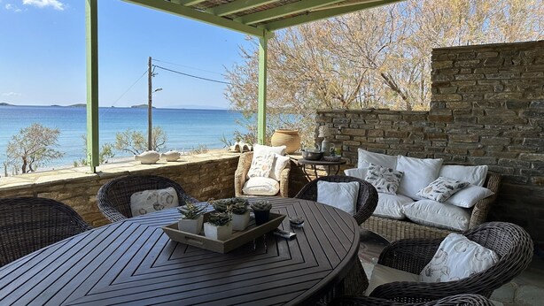 Un espace extérieur abrité, aménagé avec des meubles en osier, une table ronde sur laquelle est disposé un plateau de plantes, et offrant une vue sur la mer.