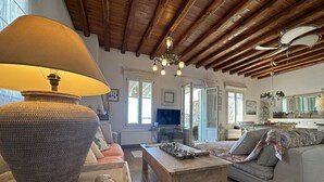 Un salon spacieux avec un plafond en bois, une grande lampe en fibres tressées, un canapé, une table basse et un téléviseur.