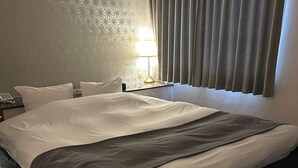 A hotel room with a large bed, a nightstand, a lamp, and a patterned wall.