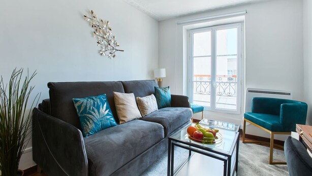 A modern living room with a grey sofa, teal armchair, and a glass coffee table with fruit.