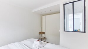 A hotel room with a neatly made bed, a wooden bench, and a large wardrobe.