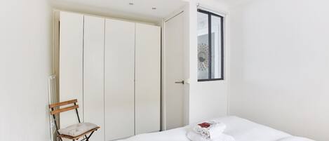 Un dormitorio con cama, una silla, un armario y una ventana.
