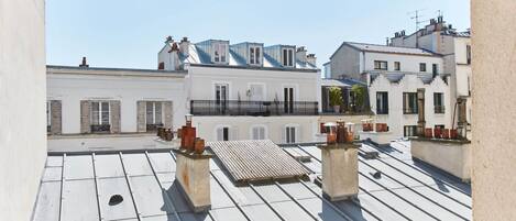 A rooftop terrace with a flat roof, white walls, and a clear sky.