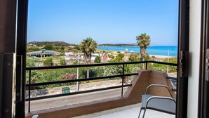 Un balcon avec vue sur une plage, des palmiers et un ciel bleu dégagé.