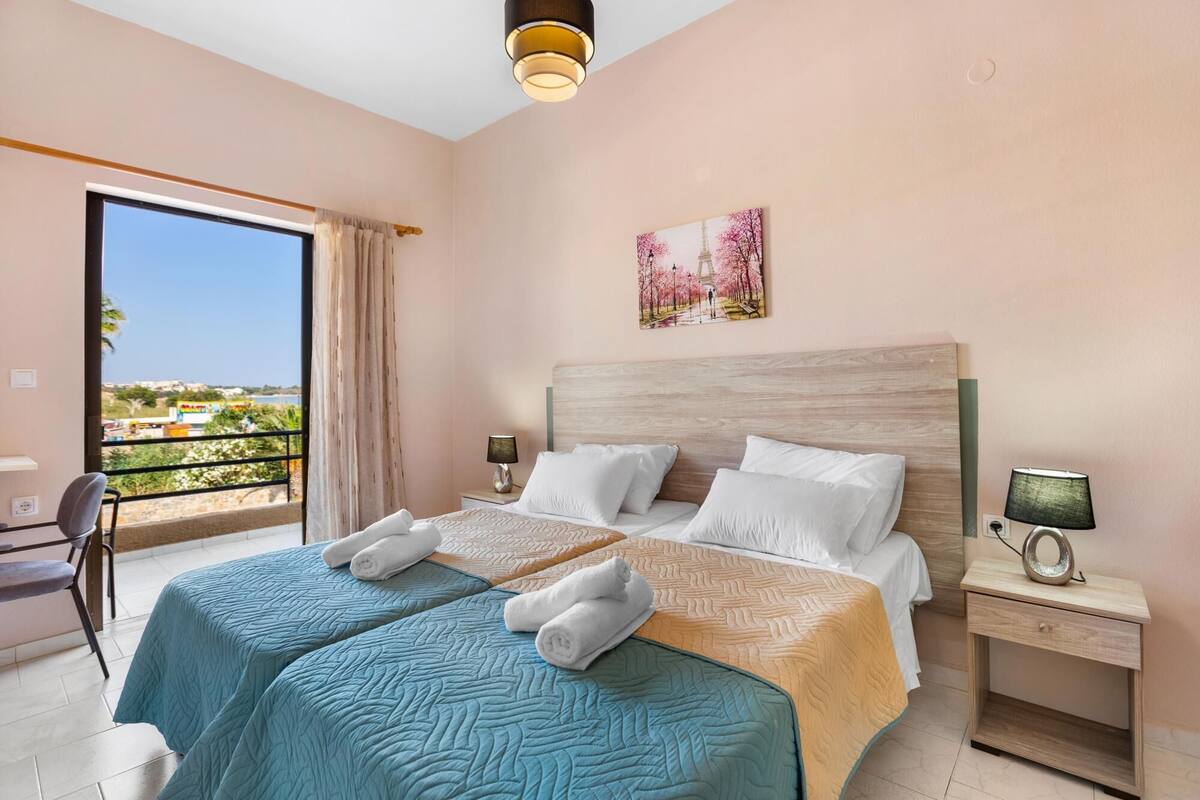A hotel room with a large bed, two bedside tables, a chair, and a balcony with a view.
