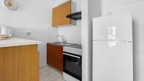 Une cuisine avec un réfrigérateur blanc, une cuisinière, un évier, des armoires en bois et une horloge au mur.