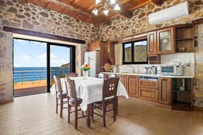 Une cuisine aux murs en pierre, aux armoires en bois et offrant une vue sur la mer.