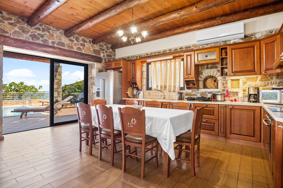 Une cuisine spacieuse avec des meubles en bois, un mur en pierre et une grande table à manger entourée de chaises.