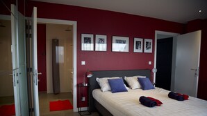 Une chambre à coucher avec un lit, une table de chevet, une porte rouge et un mur orné de tableaux.