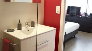 Une salle de bain moderne avec un meuble-lavabo blanc, un miroir et un mur d’accent rouge.