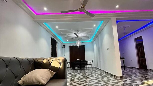 A modern living room with a sofa, a dining area with a table and chairs, and a patterned floor. - 5 Bedroom House Sleeps 12 -balcony -hired Security (Tema)