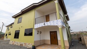 A two-story building with a balcony, a door, and a small garden area. - 5 Bedroom House Sleeps 12 -balcony -hired Security (Tema)