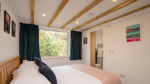Un dormitorio con techo de madera, un ventanal con cortinas, una cama con ropa de cama blanca y un cuadro en la pared.