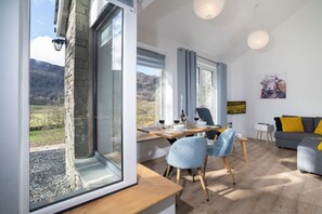 Een moderne woonkamer met een eethoek, grote ramen en uitzicht op de omgeving.