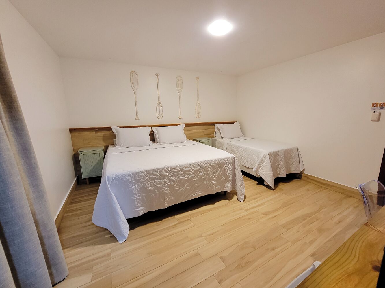 Ein Zimmer mit zwei Betten, Holzboden und einer Wand mit einer Lampe.