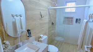 Un baño moderno con cabina de ducha de vidrio, un espejo grande y un lavabo con un florero.
