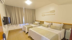 Ein Hotelzimmer mit zwei Betten, einem Fernseher, einem Holzboden und einem Fenster mit Vorhängen.