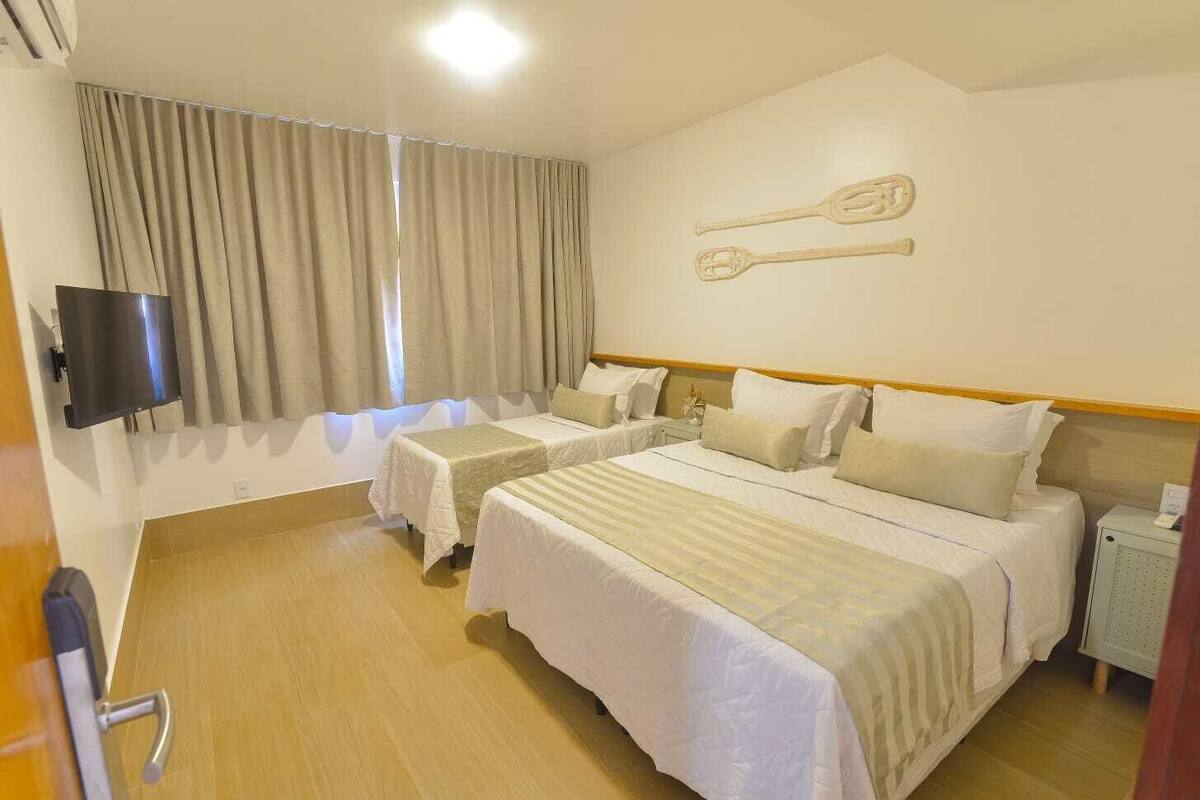A hotel room with two beds, a TV, a wooden floor, and a window with curtains.