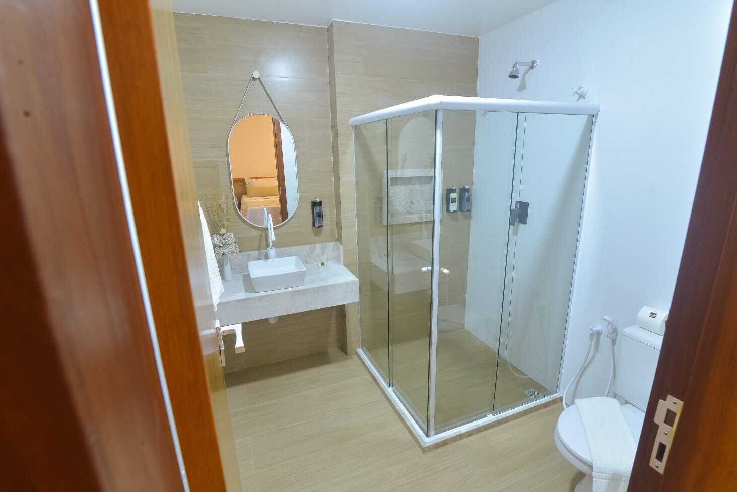 Um banheiro moderno com chuveiro em box de vidro, pia branca e vaso sanitário.
