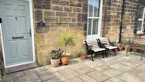 Une maison en pierre avec une porte grise, un banc et des plantes en pot.