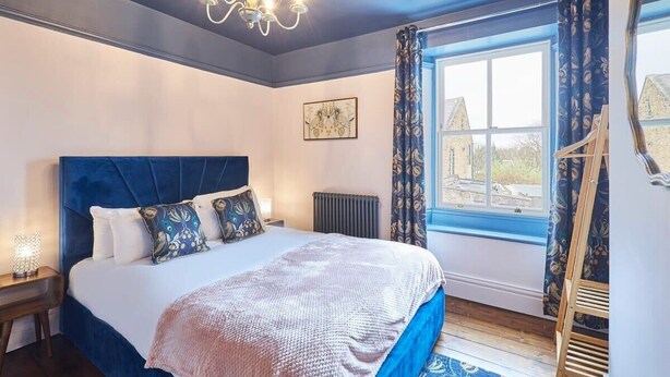 Une chambre à coucher avec un grand lit, un lustre, une fenêtre avec des rideaux et une vue sur un bâtiment à l’extérieur.