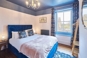 Un dormitorio con una cama grande, un candelabro, una ventana con cortinas y vistas a un edificio.
