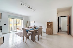 A modern living room with a dining area, a sliding glass door to a balcony, and a wooden cabinet. - Monopoli Beach House 200 m From the sea (Monopoli)