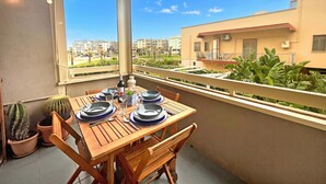 A balcony with a wooden table set for dining, potted plants, and a view of residential buildings. - Monopoli Beach House 200 m From the sea (Monopoli)