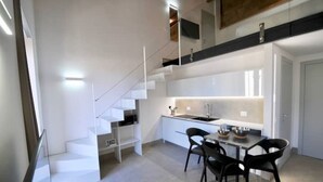 Une cuisine moderne avec un coin repas, des meubles blancs et un escalier menant à l’étage supérieur.