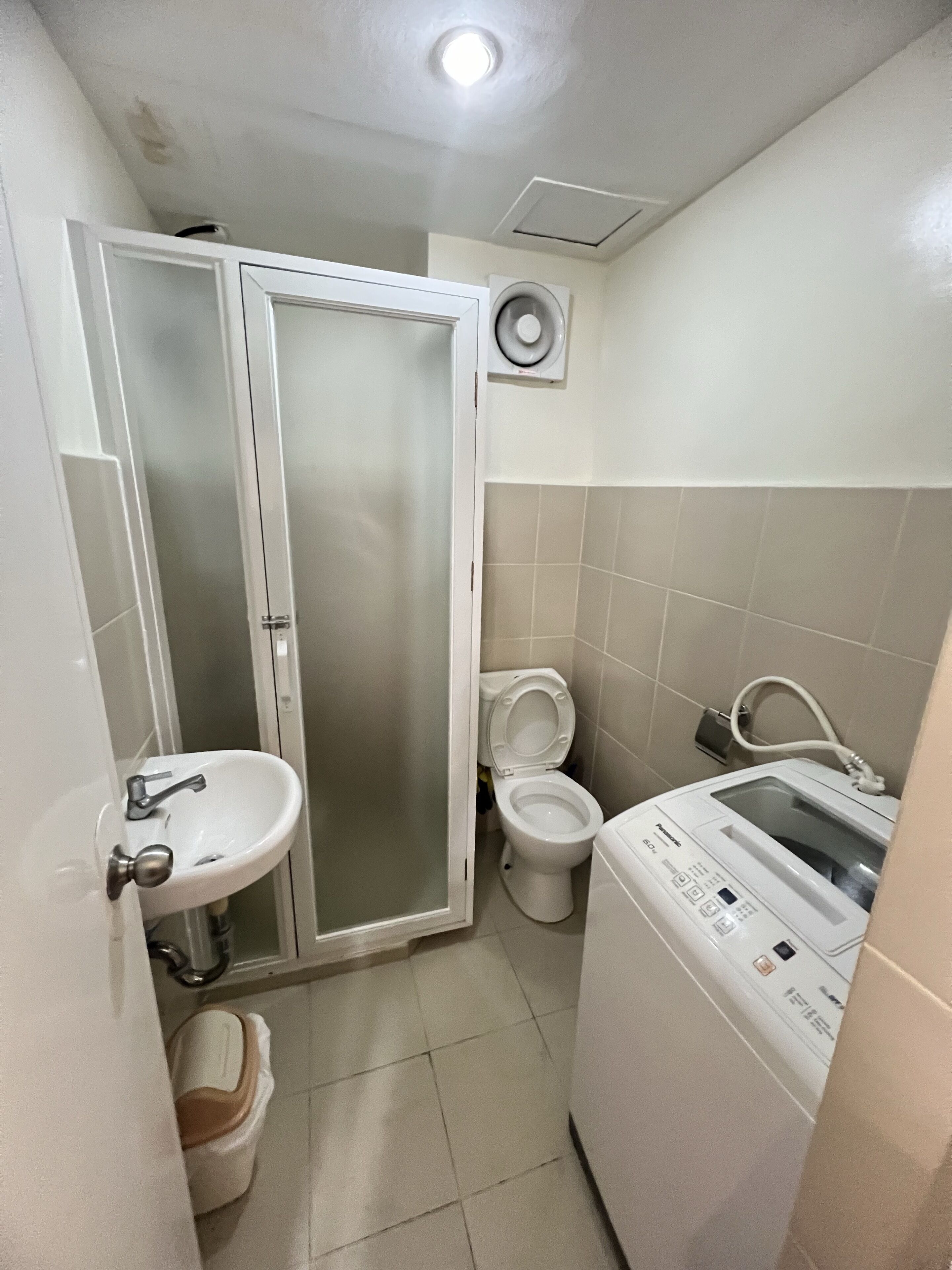 A compact bathroom with a toilet, a sink, a washing machine, and a shower enclosure.
