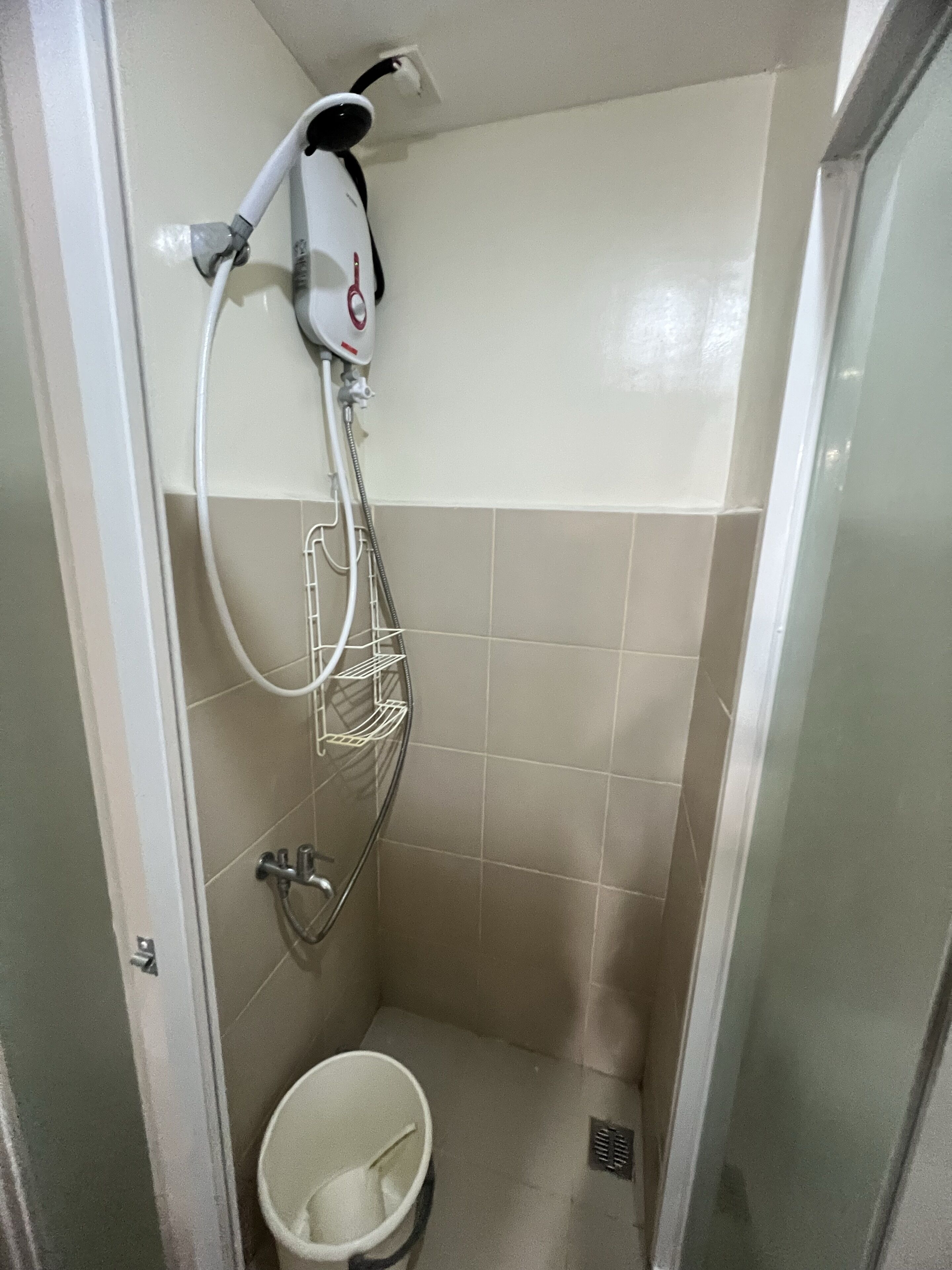 A small, enclosed shower area with a handheld showerhead, a metal rack, and a white bucket.