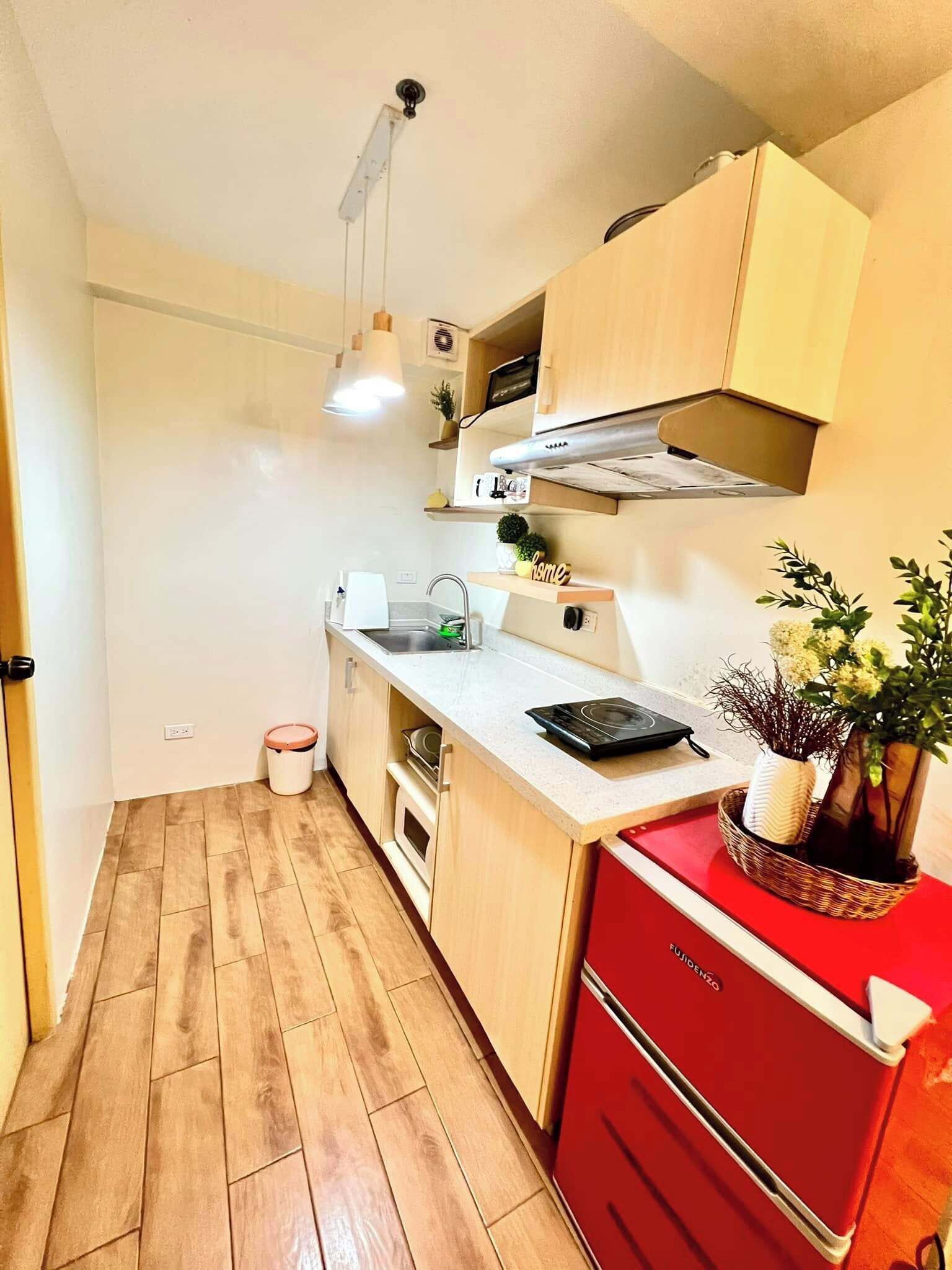 Une cuisine de taille réduite, avec un plancher en bois, un réfrigérateur rouge et un petit plan de travail.