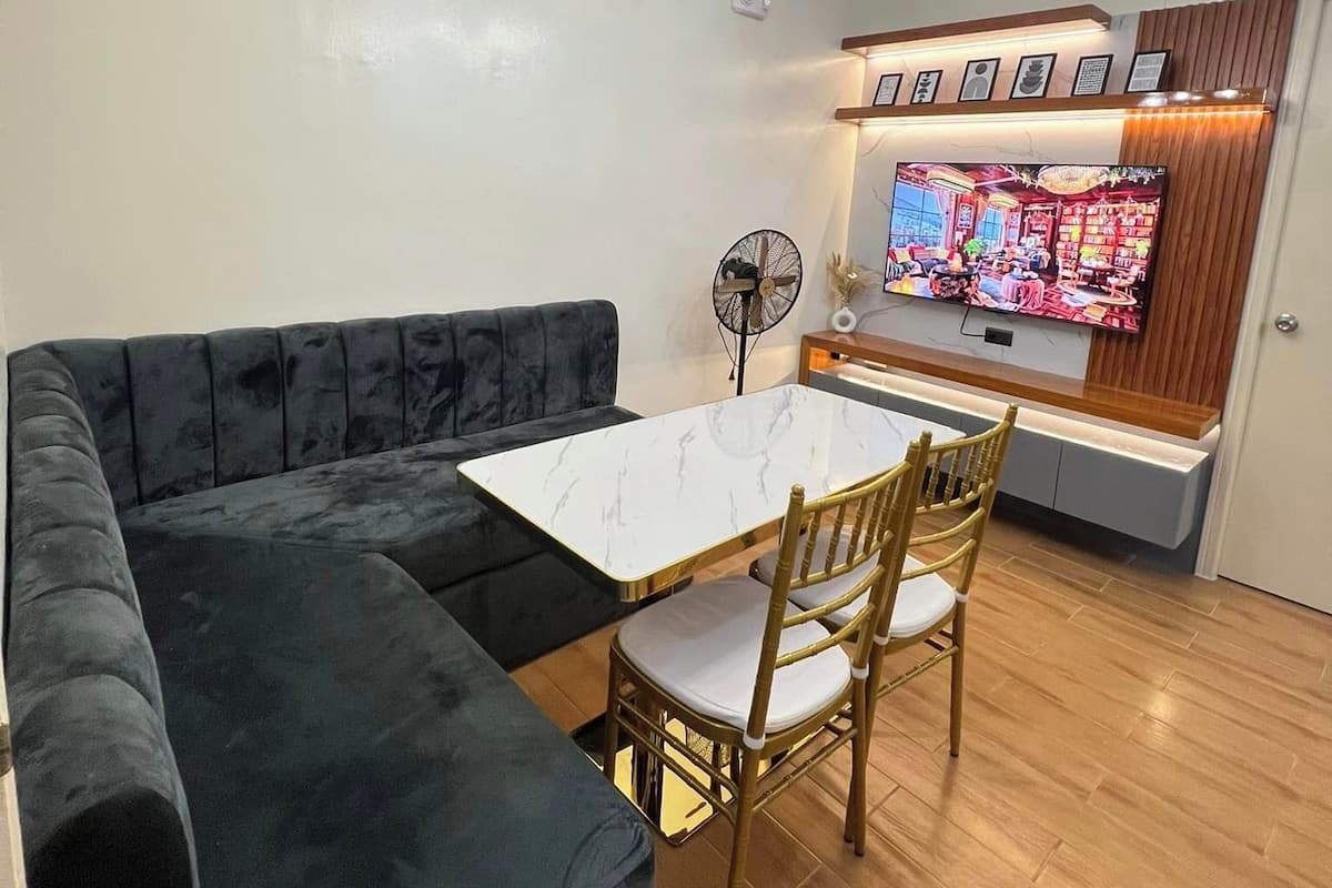 Una sala moderna con un sofá modular, una mesa de comedor con sillas, un televisor de pantalla plana montado en un mueble de madera y un ventilador de techo.