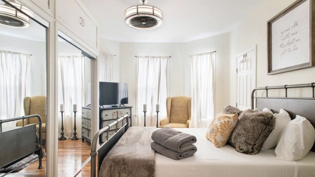 A hotel room with a bed, a chair, a television, and a bedside table. - Cozy 3 bedroom - Free Parking, close to buses.  (Boston)