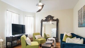 A living room with a TV, green armchairs, a blue sofa, a mirror, and a ceiling fan. - Cozy 3 bedroom - Free Parking, close to buses.  (Boston)