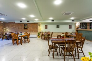 Un comedor amplio con varias mesas y sillas de madera, una pared de ladrillo y una pared verde decorada con cuadros.