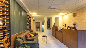 A modern hotel lobby with a sofa, a small round table, a wine rack, and a reception desk. - LILEO Hotel (Kutaisi)