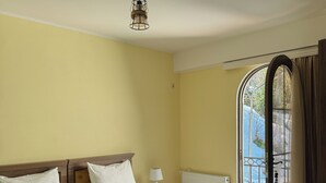 A double bed with two pillows, a bedside table with a lamp, and a window with curtains. - LILEO Hotel (Kutaisi)