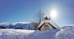 Un paysage enneigé avec une structure ressemblant à une église, surmontée d’une croix, entouré de montagnes et sous un ciel dégagé.