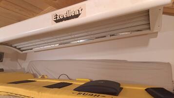 Una habitación con una cama cubierta con ropa de cama amarilla, un almohadón negro y un cabecero negro. Se observa una unidad de aire acondicionado blanca con la etiqueta 'Excelente' sobre la cama.