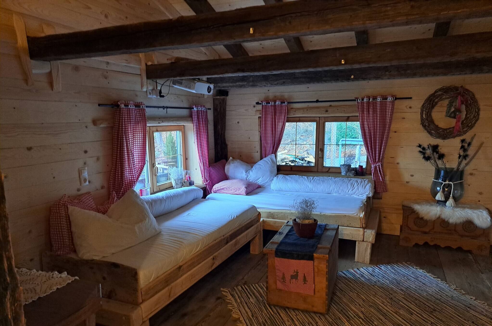 Ein gemütliches Blockhauszimmer mit zwei hölzernen Betten, karierten Vorhängen, einem gewobenen Kranz und einem rustikalen Holztisch.