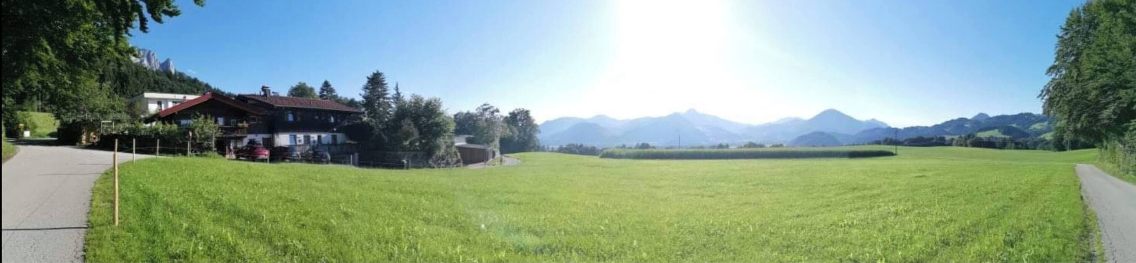 Un campo cubierto de hierba con un edificio a la izquierda y montañas al fondo.
