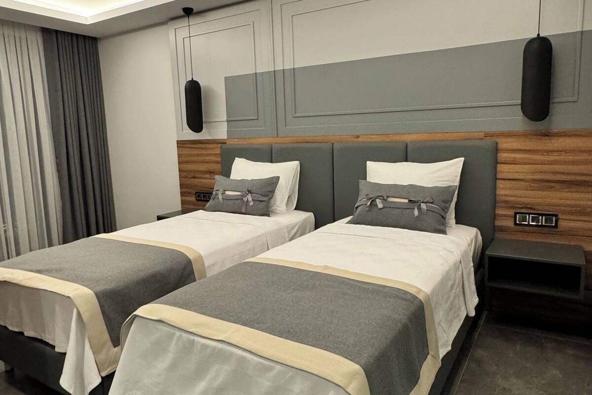 A modern hotel room with two beds, a wooden headboard, a ceiling light, and a nightstand.