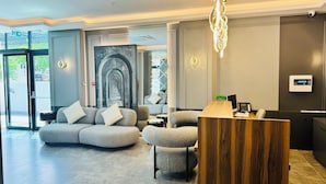 A modern lobby with a grey sofa, a wooden reception desk, and a large wall mural. - Telmessos City Hotel ADULTS ONLY (Fethiye)