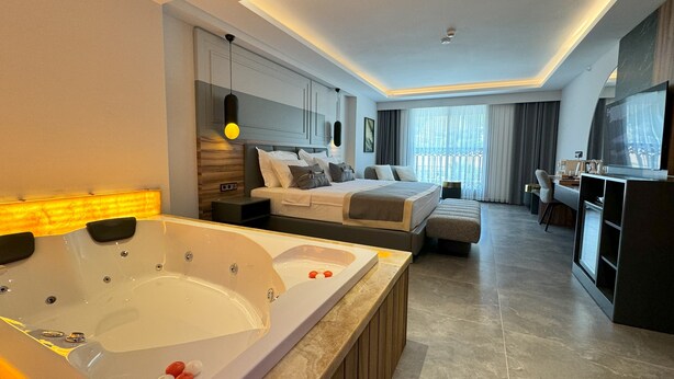 A modern hotel room with a large bathtub, a bed, a desk, and a television. - Telmessos City Hotel ADULTS ONLY (Fethiye)