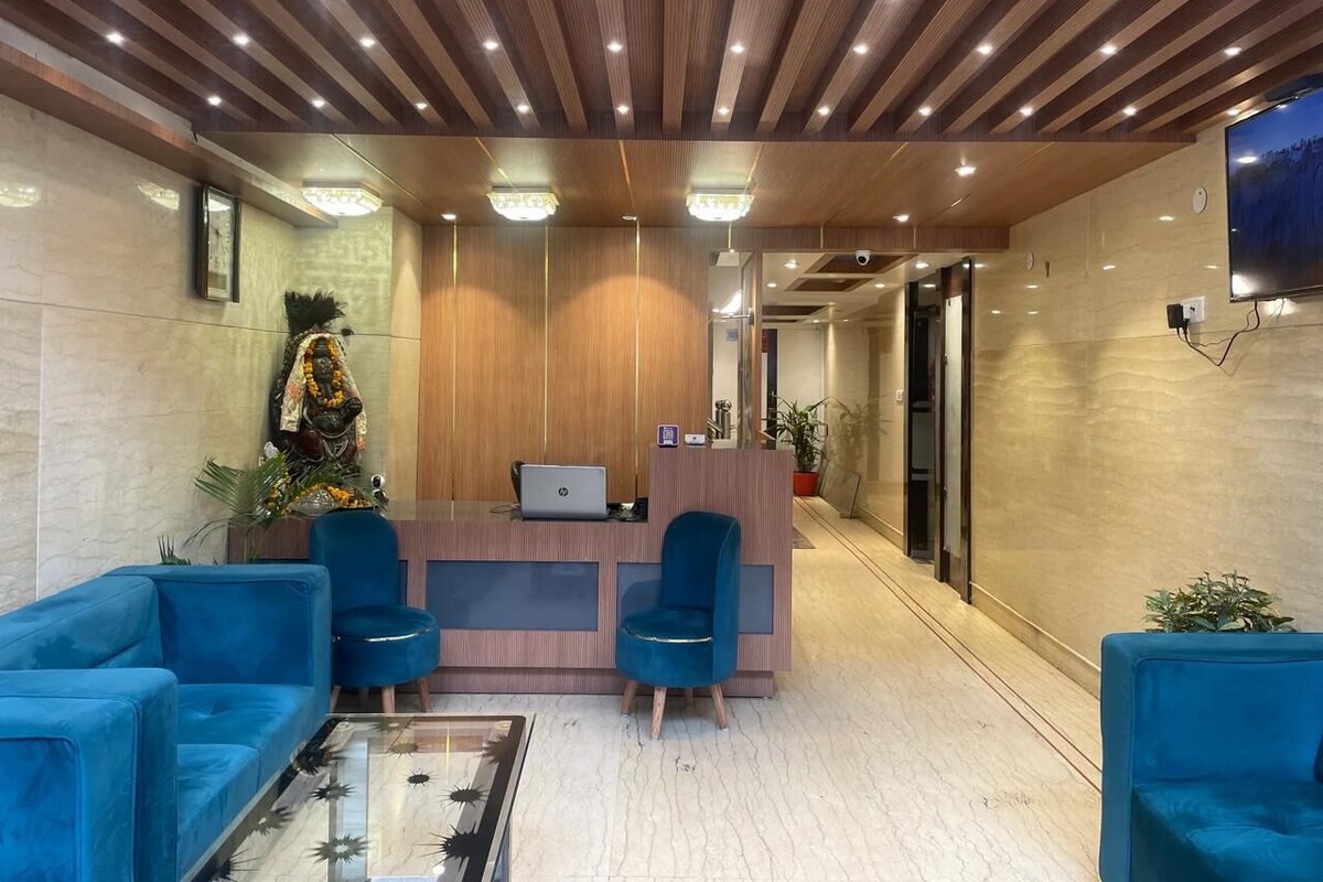 Un área de recepción con techo de madera, un mostrador, dos sillas azules, una computadora portátil y una mesa de centro de vidrio.