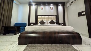 A bedroom with a large bed, a ceiling fan, an air conditioning unit, a blue chair, and a small table. - Hotel Galaxy (Reasi)